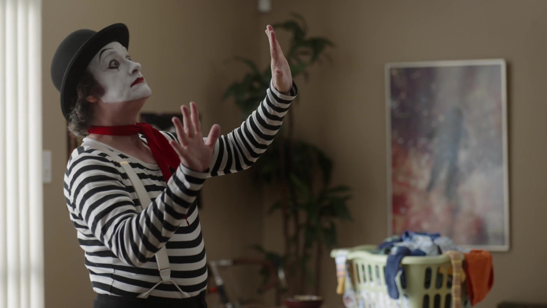 A mime in a striped shirt holds both hands against an imaginary barrier in an apartment.