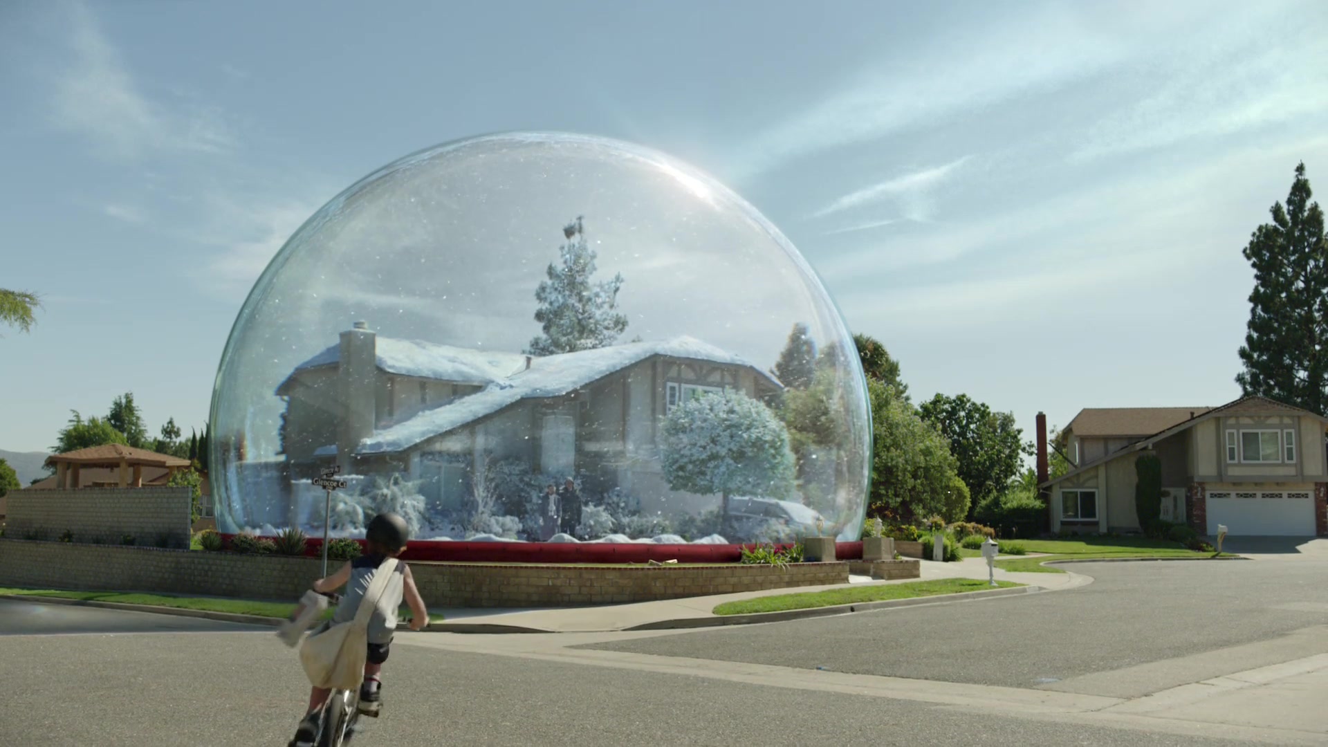 A house enclosed in a giant snowglobe beside a sunny suburban street.