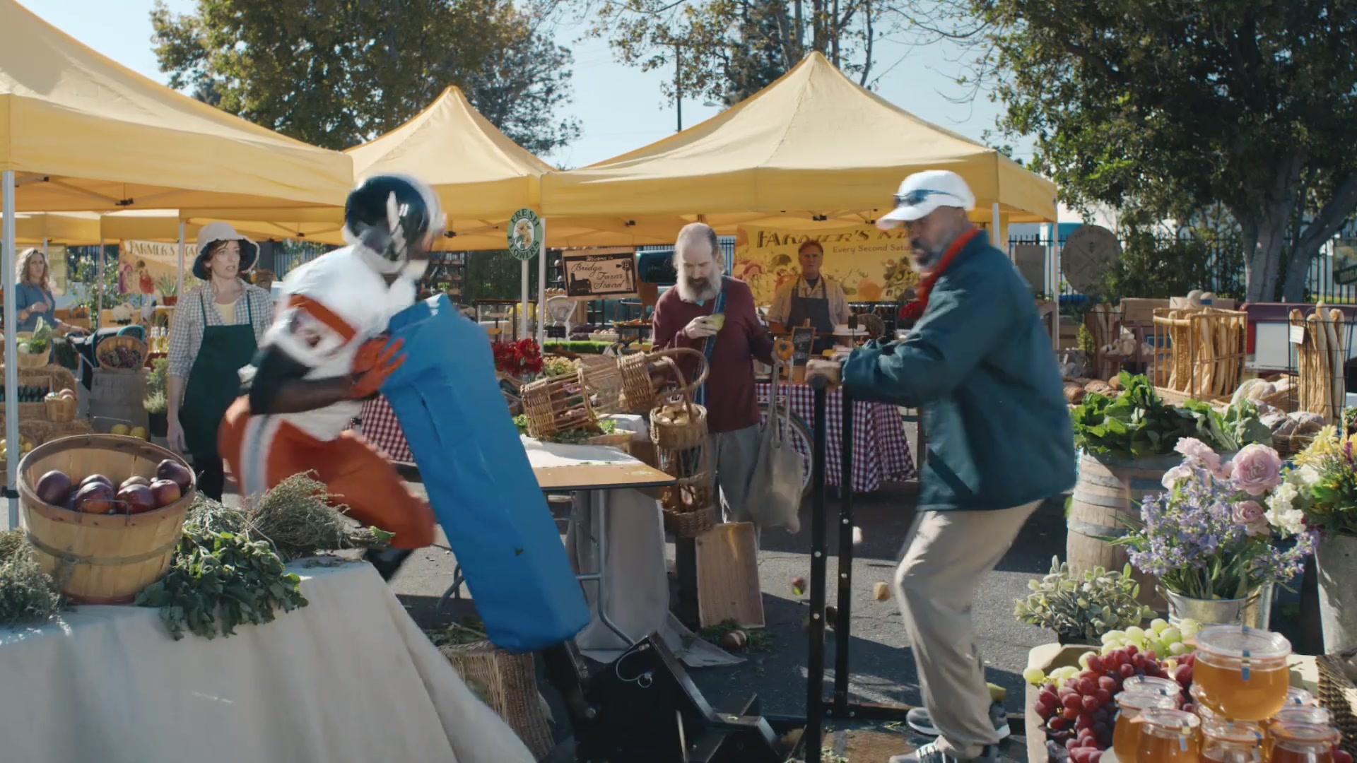 Always in Season — Football player and coach crash through a colorful farmers market