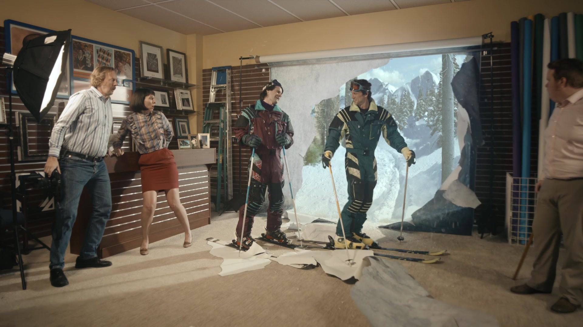 Smile and Say Skis — Skiers emerge through photographic backdrop with mountain visible through torn wall