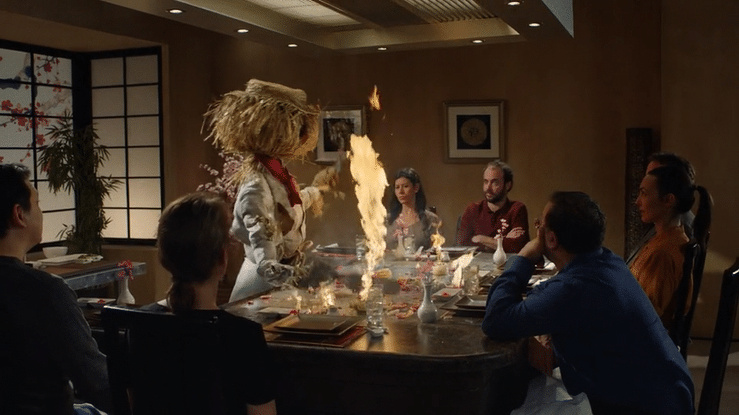 A scarecrow cooks over a flaming hibachi grill while diners watch.