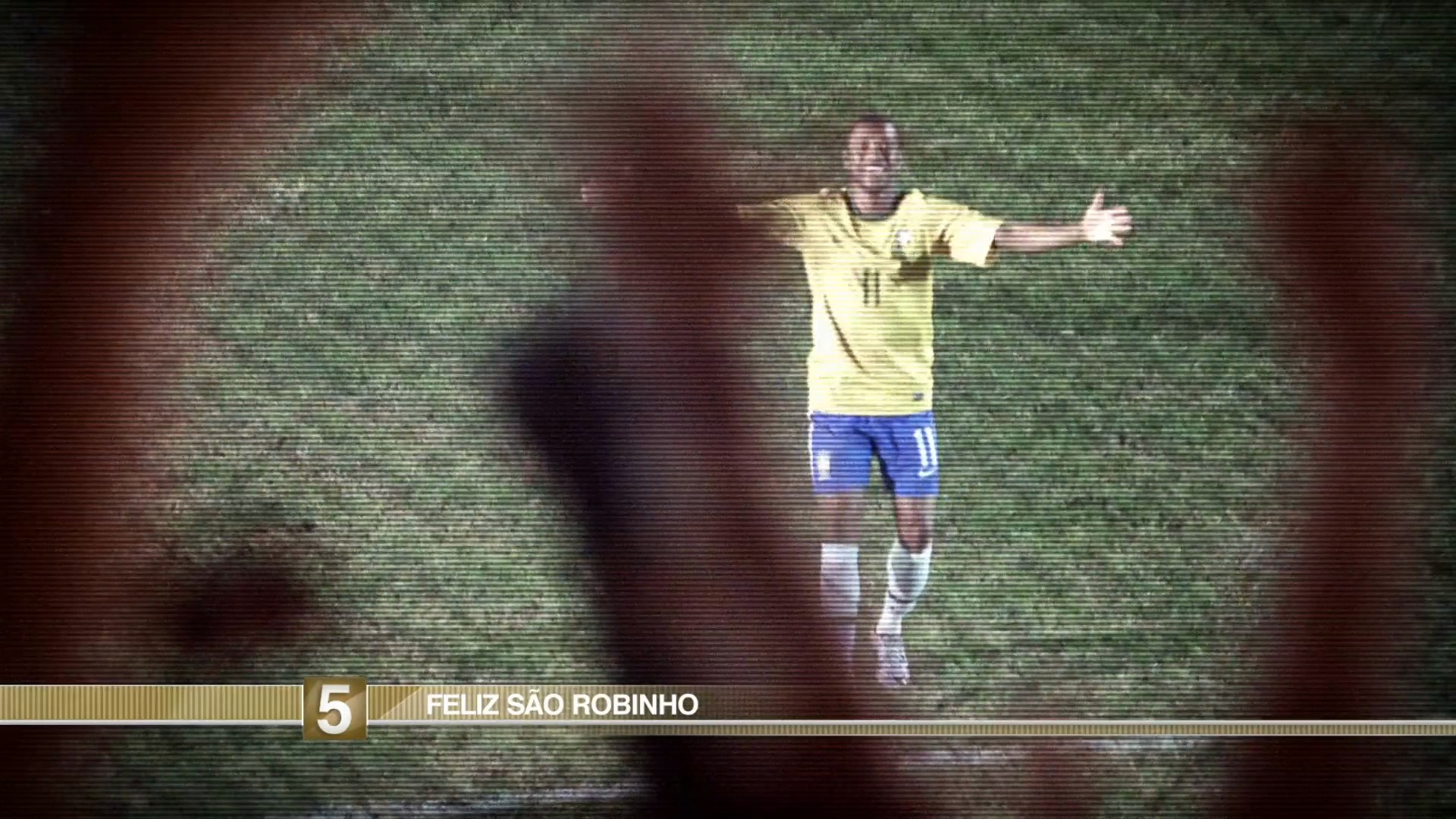 São Robinho — the footballer raises his arms on the pitch beneath the Feliz São Robinho television caption